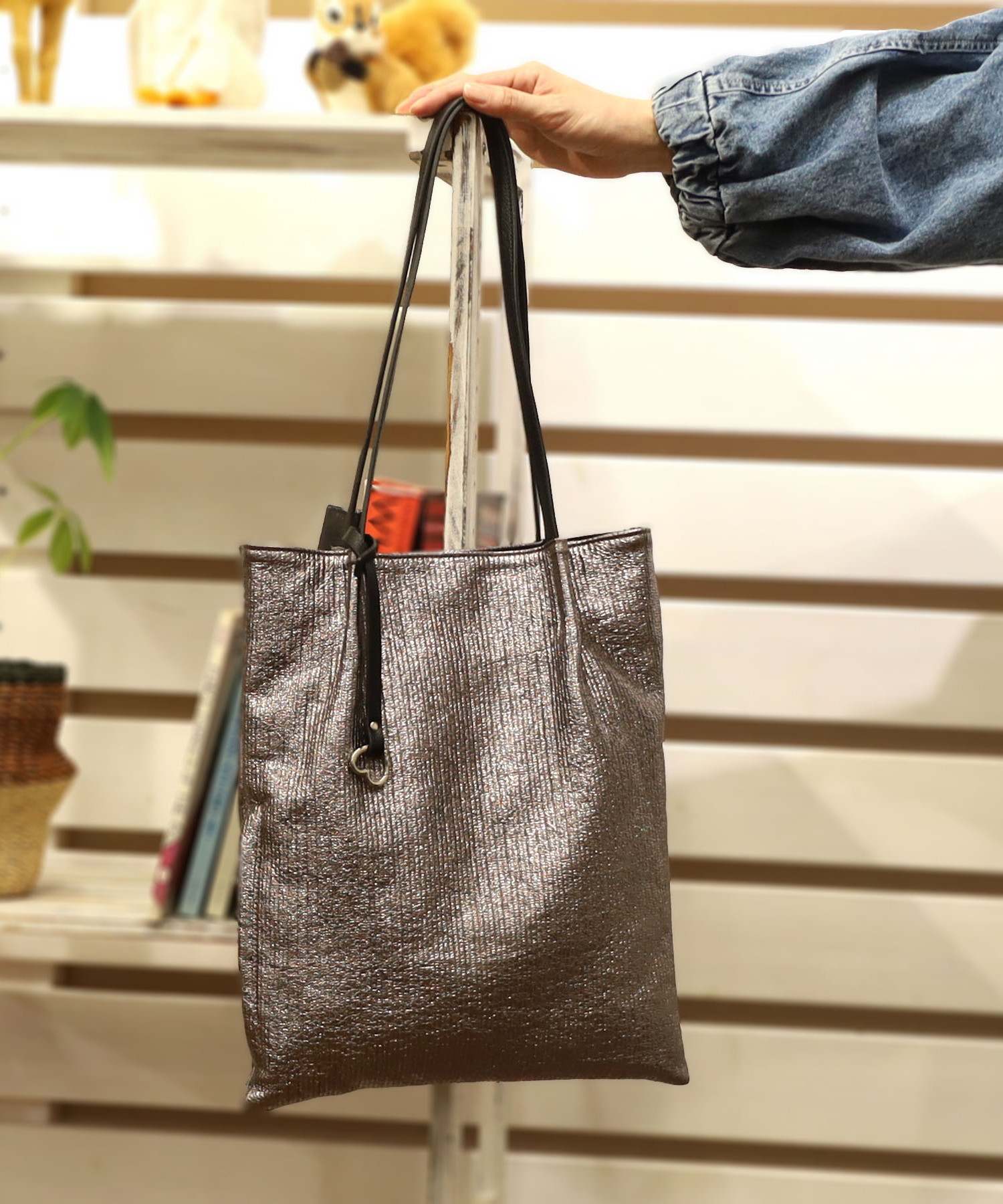 シンプルなつまみハンドルデザインの縦型トートです。ハートのカラビナチャームがポイント。サイドに何かと使えるファスナーポケット付き。生地感のあるメタリック素材が大人っぽい。