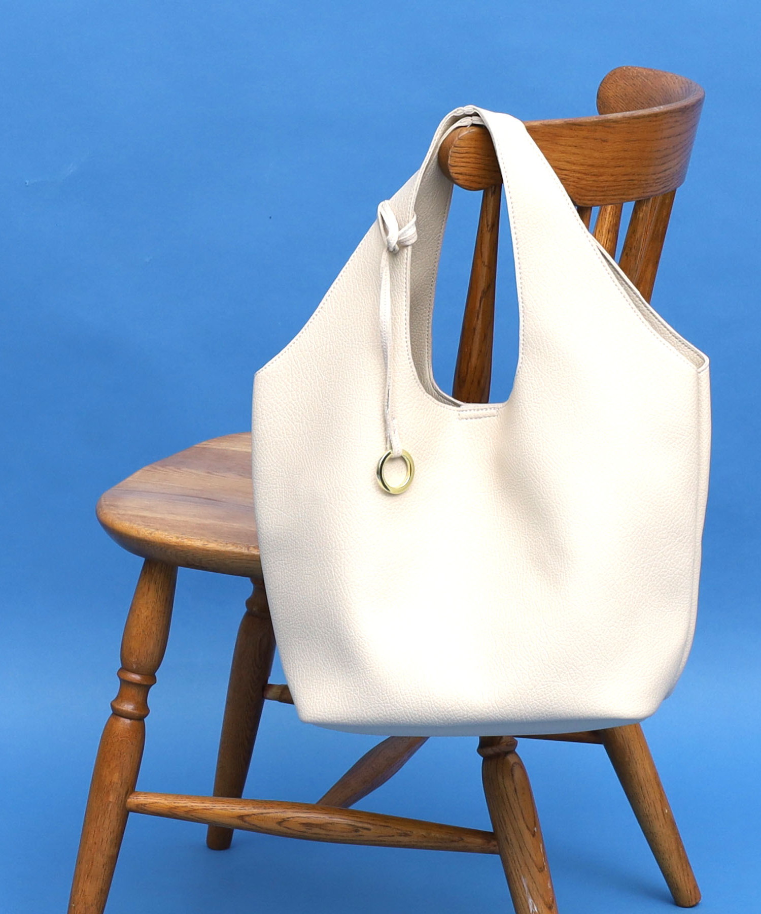 定番素材のソフトフェイクレザーを1枚で使用したBAGです。すっきりとした見た目のくり手トートに仕上がりました。ハンドルは太めですので肩に優しくフィットします。金具チャームがワンポイントになっております。内装は裏地を付けず、メッシュ素材などで４か所ポケットが付いておりますので収納力あり。バッグの容量はB5サイズ程度の大きさのものが収納可能で、お出かけに必要なものはしっかり入ります。ON/OFFで活躍するシンプルデザインです！